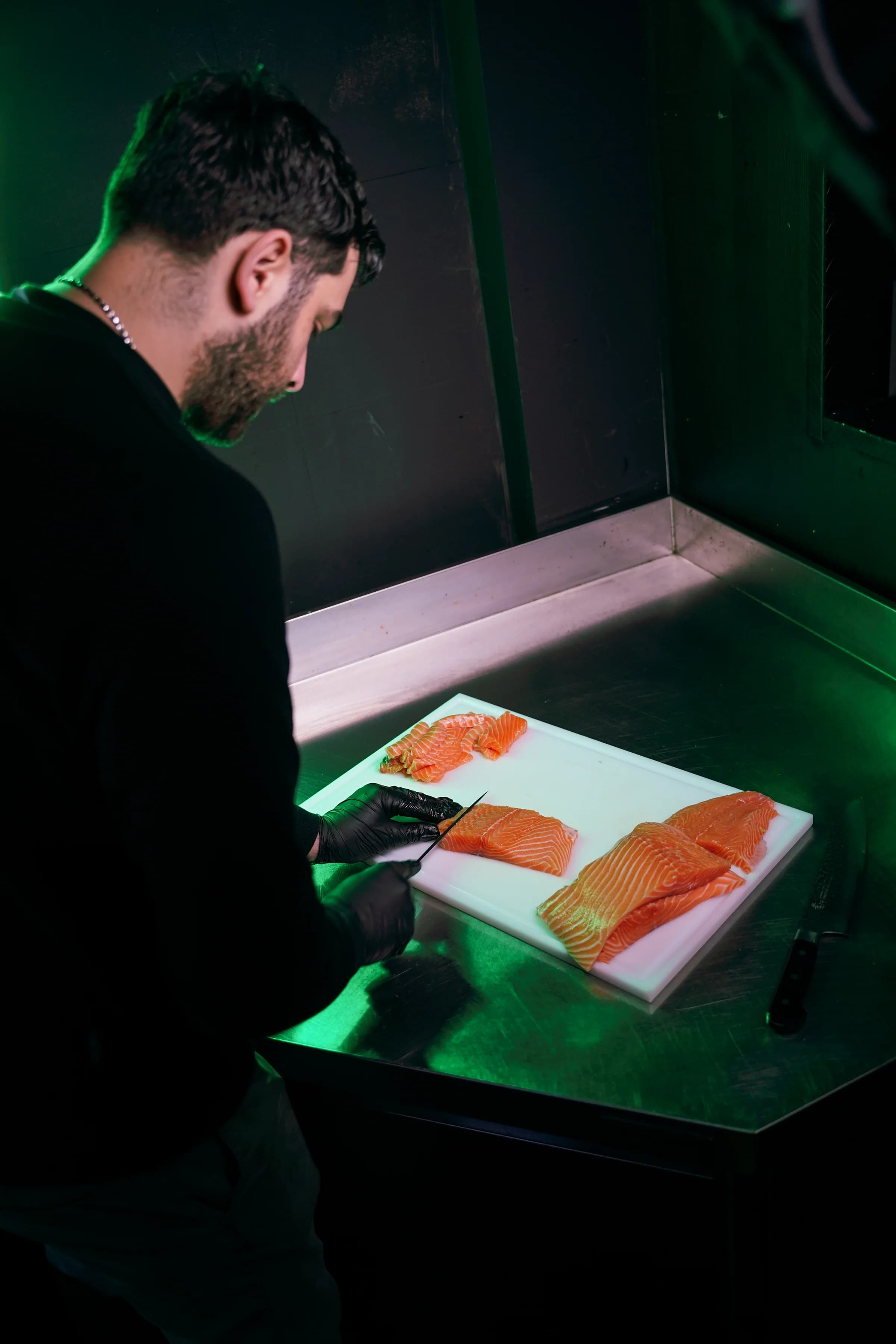 Een medewerker snijdt verse zalm op een witte snijplank in groen licht